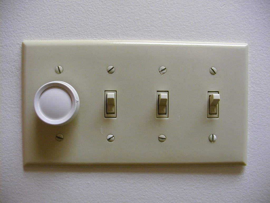 Light switch plate with one dial three switches in on position are shown on a white wall