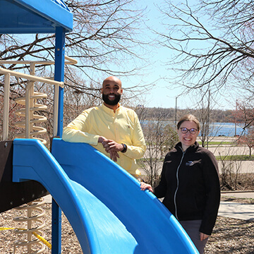 IOCP Staff member Abdi and Three Rivers Park staff member Heather stand next to slide in Parkers Lake in Plymouth, MN