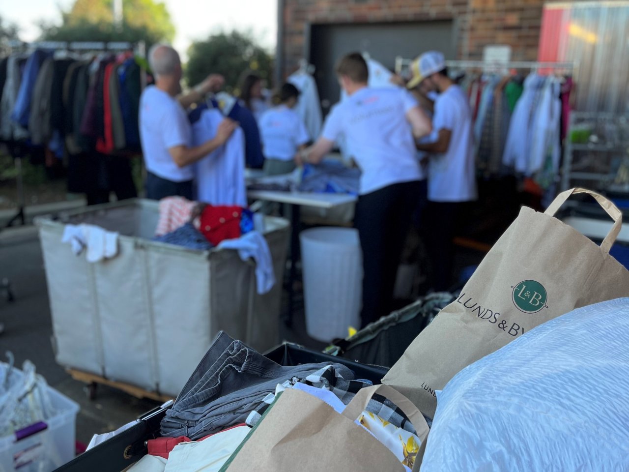 Background of volunteers sorts through clothes at IOCP donation door. More items in foreground.
